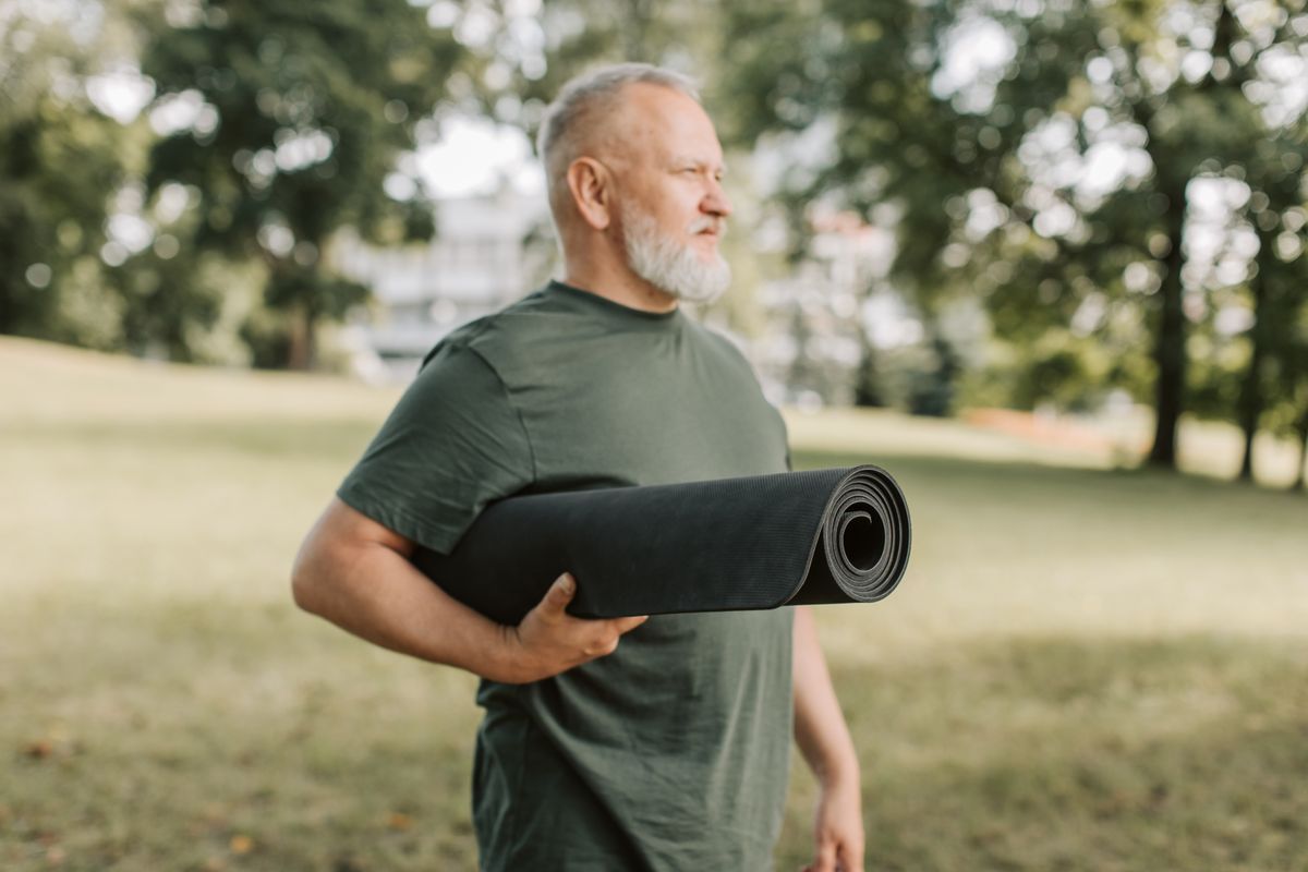 Man van rond de vijftig met een yogamat onder zijn arm in een park