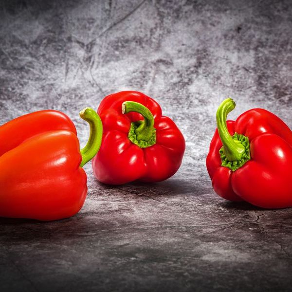 Drie rode paprika's op een stenen ondergrond