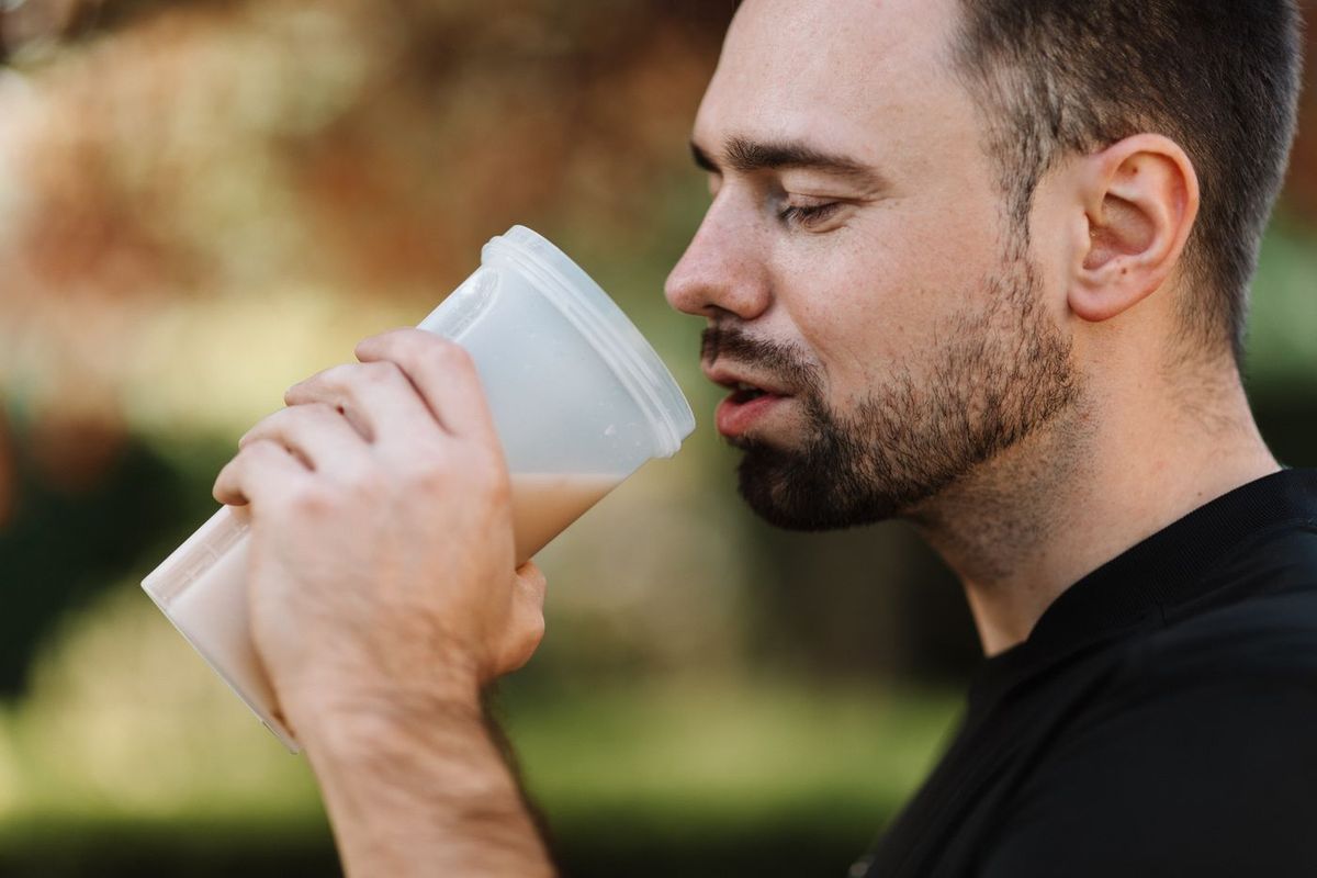 Man met baard die buiten uit een beker een smoothie drinkt