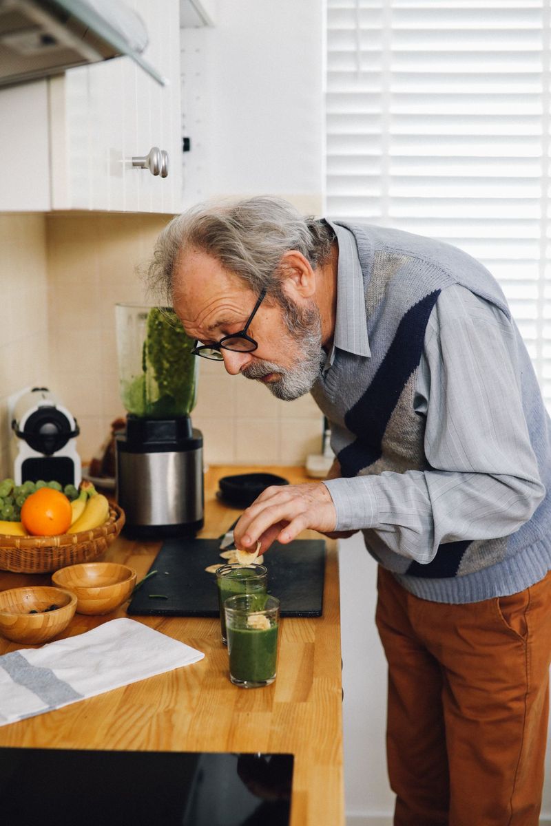 Oudere man die in zijn keuken een groene smoothie maakt