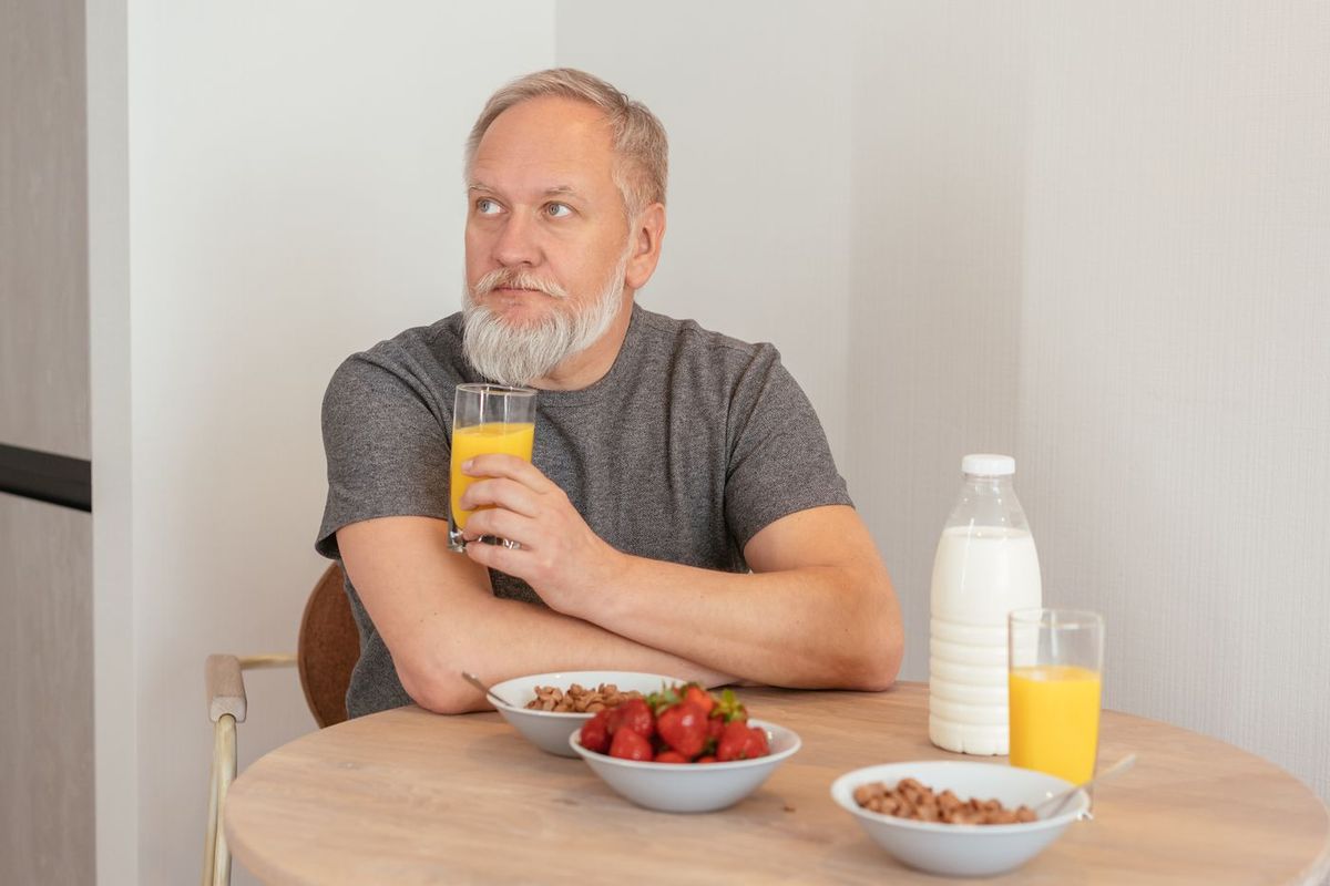 Man aan de keukentafel met een glas en een ontbijt
