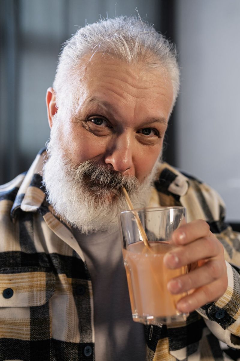 Oudere man met grijze baard die met een rietje een smoothie drinkt